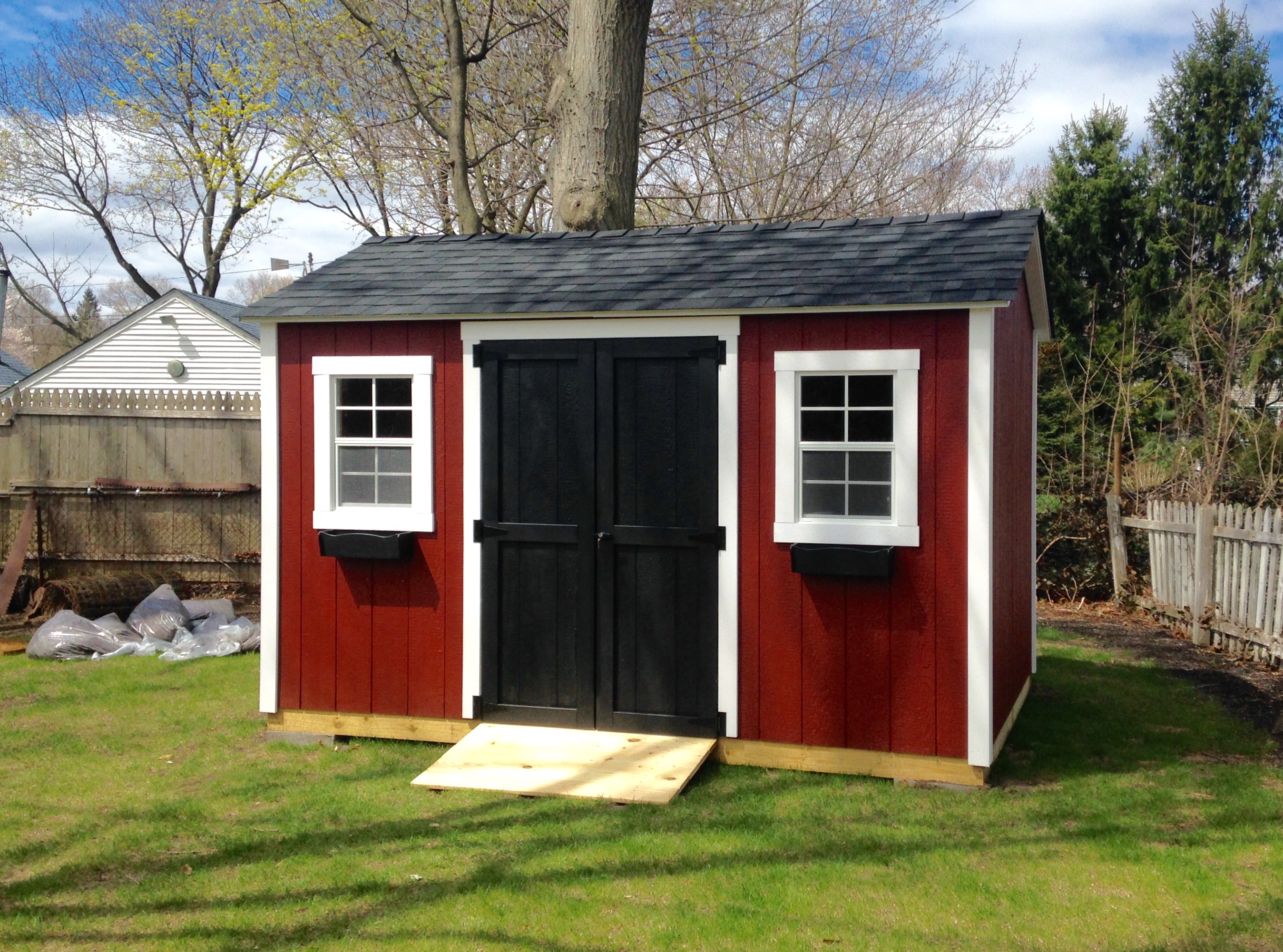 Red garden shed with white trim, black double doors, and two front windows.
