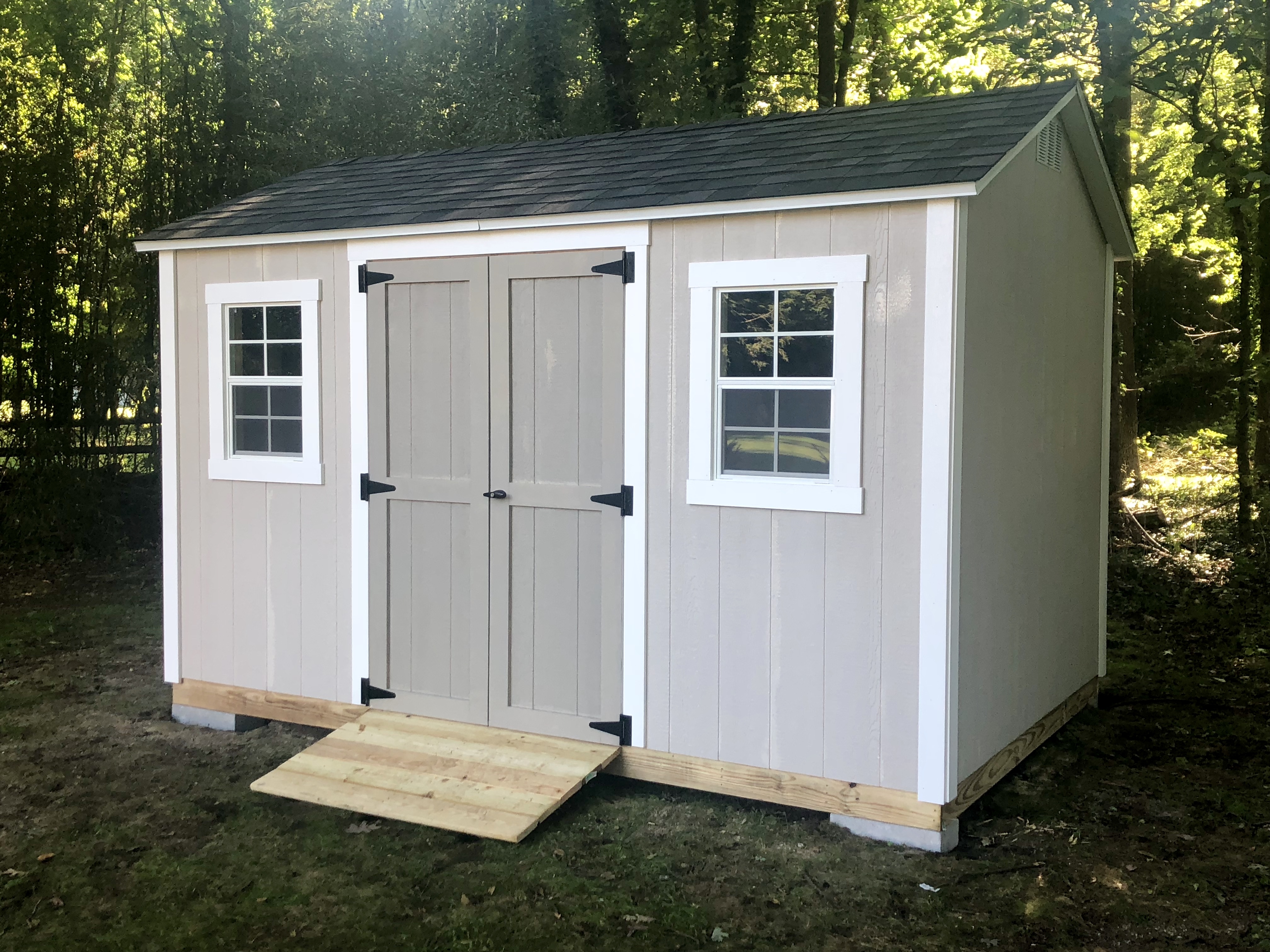 Light gray gable-roof storage shed with white trim, double doors, a front window, and a wooden entry ramp.